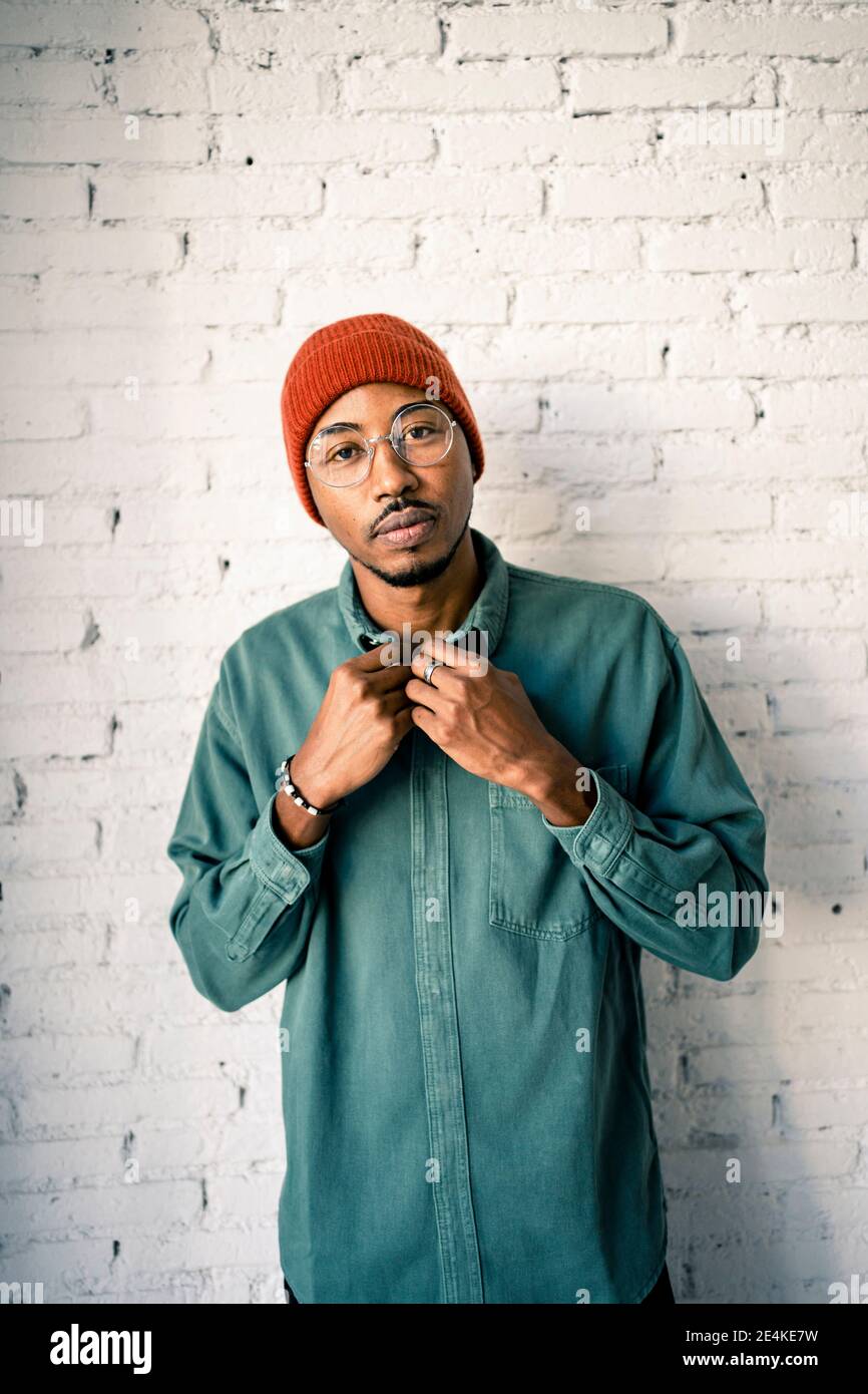 Uomo sicuro che indossa un cappello a maglia contro una parete di mattoni bianchi Foto Stock