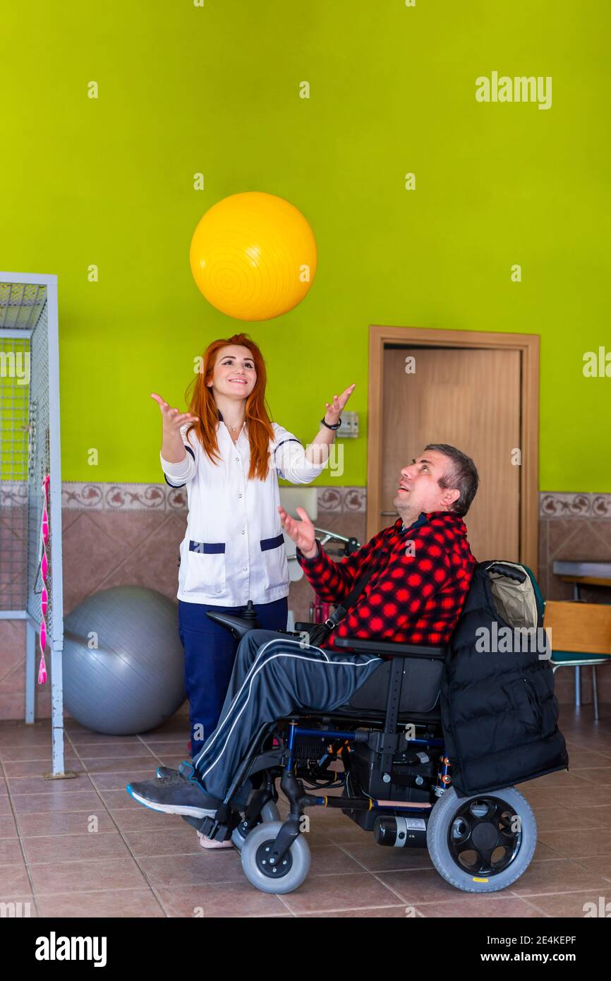 Giovane infermiera femminile e uomo disabile che gioca con palla fitness in centro di riabilitazione Foto Stock