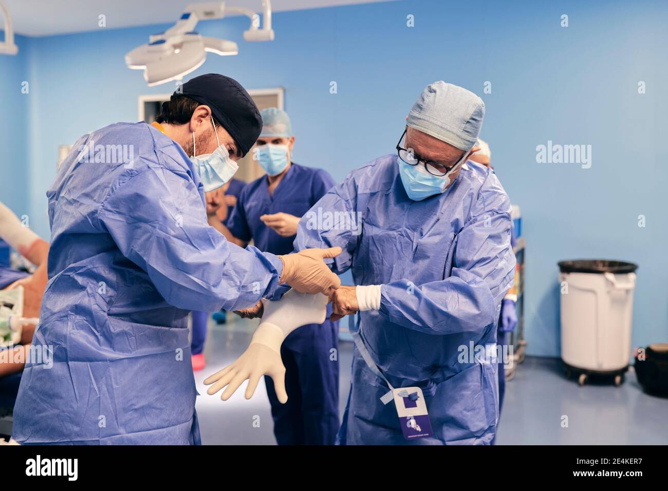 Assistente che aiuta il medico a indossare guanti protettivi mentre si sta in piedi sala operatoria Foto Stock