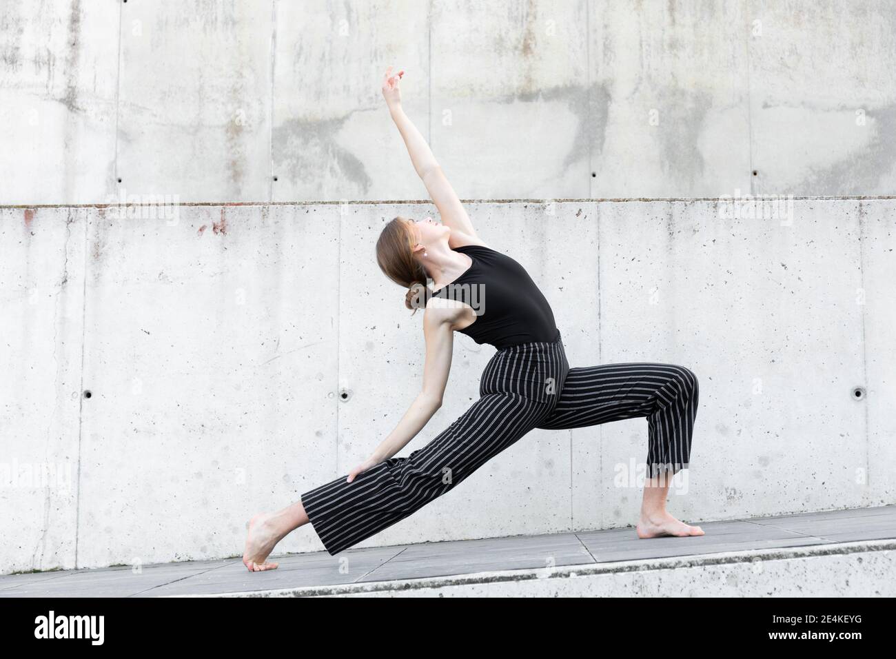 Ballerina in pantaloni a righe nere davanti alla parete in cemento Foto Stock