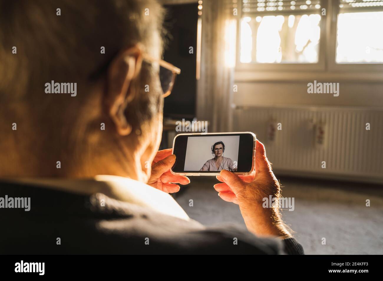 Uomo anziano che prende il consiglio dal medico generale femminile sul video chiama tramite smartphone in salotto Foto Stock