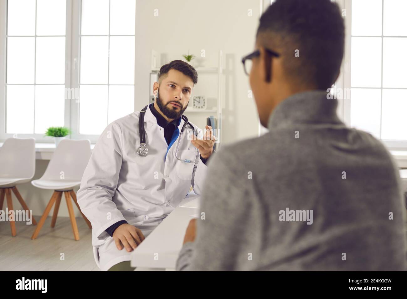 Uomo medico terapeuta seduta e parlando con paziente uomo nero in clinica Foto Stock