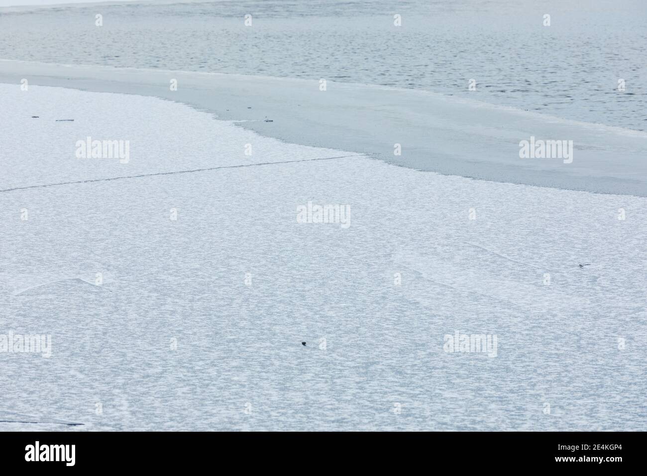 Superficie del lago parzialmente congelata e neve durante il giorno d'inverno Foto Stock