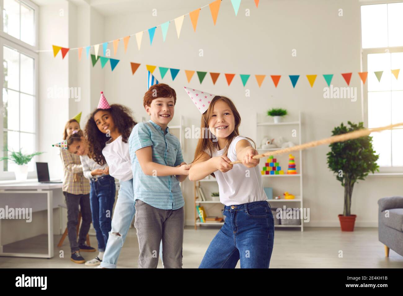 Una squadra di ragazzi e ragazze si diverte e gioca un gioco di tug-of-war in una festa per bambini. Foto Stock