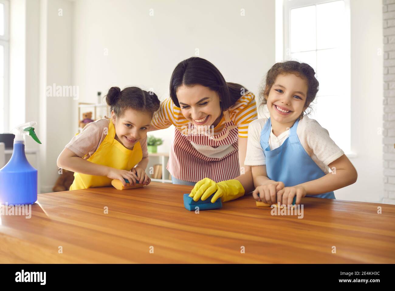 Carino piccole figlie imparare a fare le faccende di famiglia e aiutare la madre lava il tavolo Foto Stock