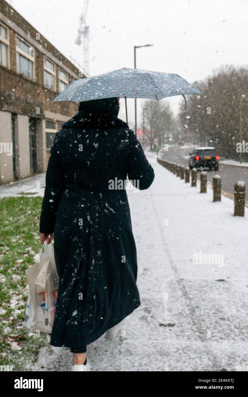 Una donna pedonale cammina con attenzione indietro dal supermercato nella neve. Il marciapiede è coperto di neve poiché la sabbia è applicata solo alle strade nonostante le condizioni meteorologiche avverse. Londra. Meteo Regno Unito. Foto Stock