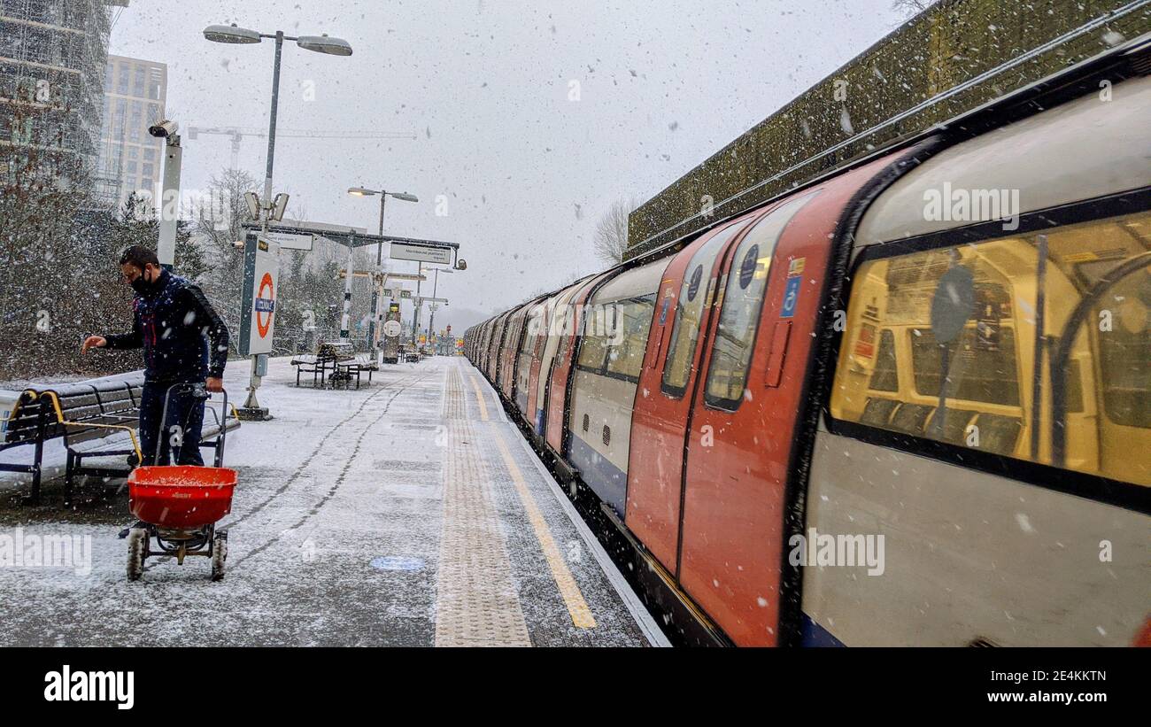 Il lavoratore della TFL applica in fretta il sale granato alla piattaforma ferroviaria della stazione della metropolitana di Colindale mentre nevica il 24 gennaio 2021. I trasporti per Londra non sono preparati per il maltempo sulla rete metropolitana di Londra, nonostante gli avvertimenti meteorologici del MET Office siano in atto per le forti nevicate. Colindale, Londra. Regno Unito Meteo. Foto Stock