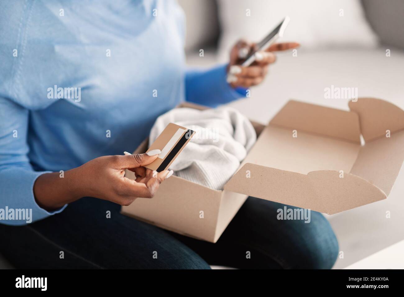 Donna nera seduta con box, carta di credito e smartphone Foto Stock