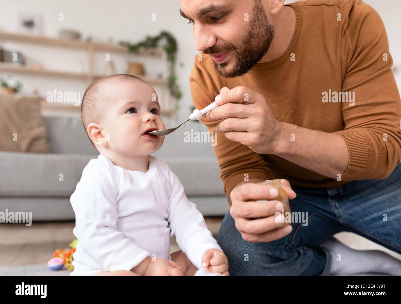 Loving Young Padre Spoon nutrire il suo bambino seduto al chiuso Foto Stock