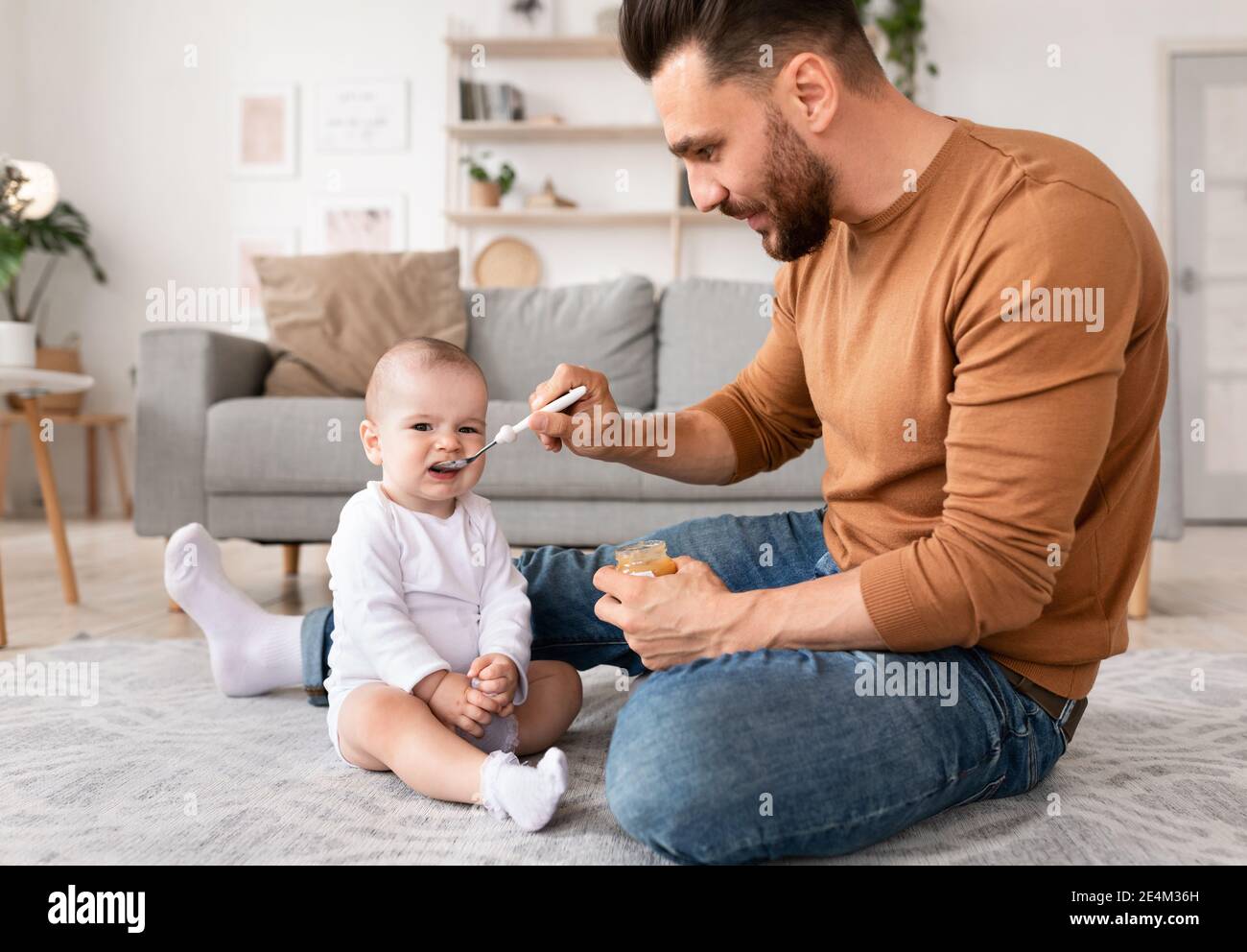 Il giovane padre alimenta il bambino con il cucchiaio seduto a casa Foto Stock
