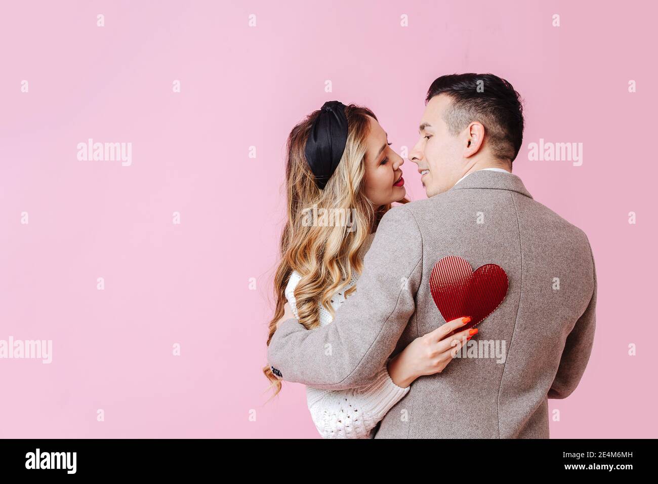 Coppia coccole in bella posa, la ragazza tiene un San Valentino dietro la schiena del ragazzo Foto Stock