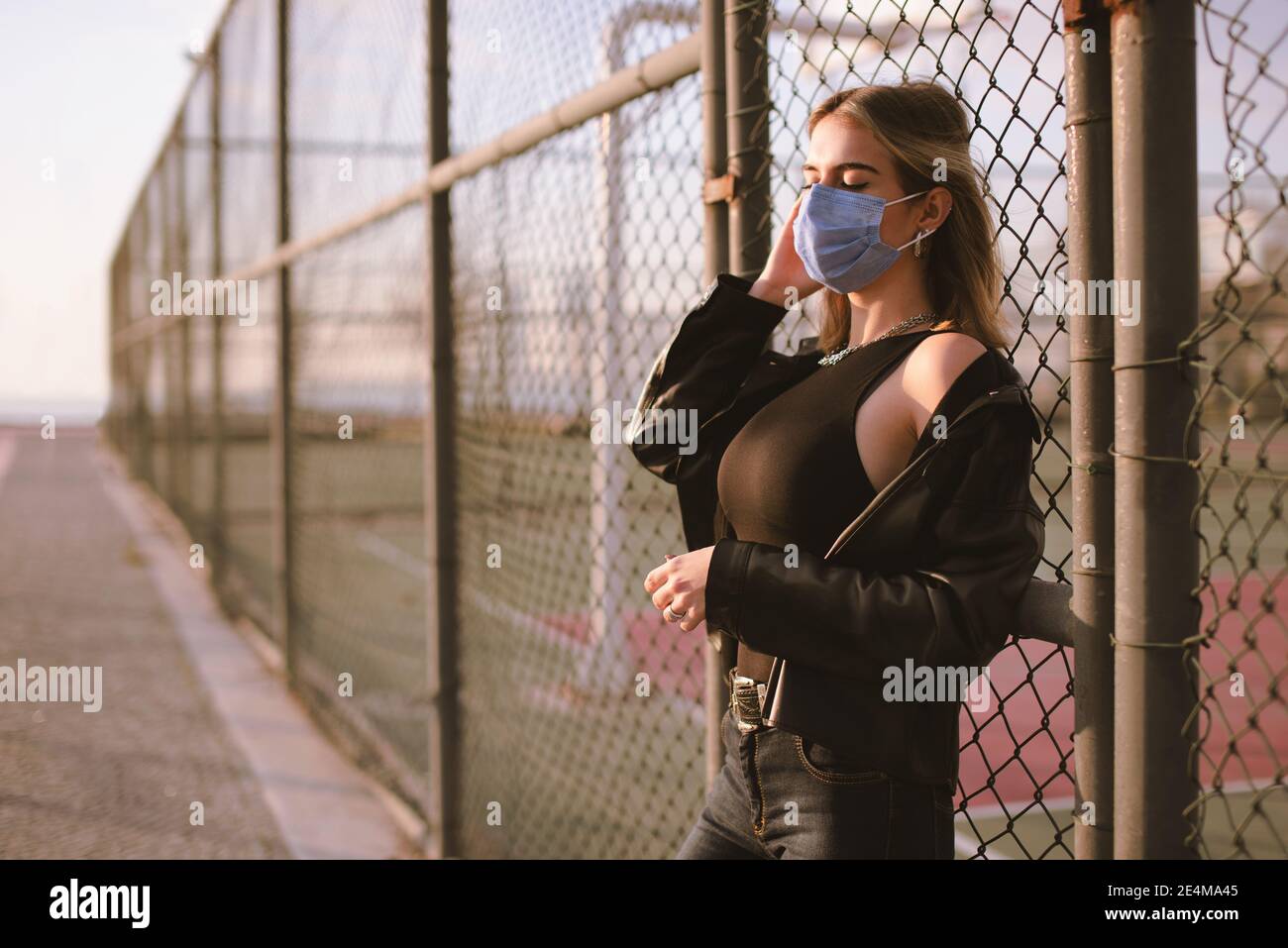 Ritratto di una ragazza adolescente con una maschera medica viso sulla strada, e pendente a una recinzione. Foto Stock