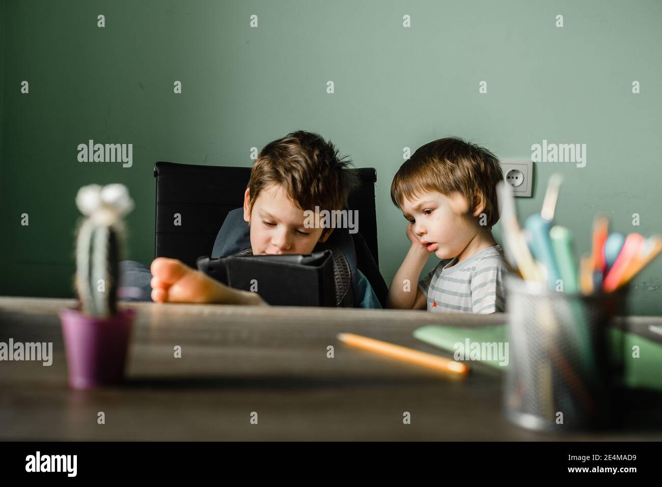 Ragazzo junior con suo fratello che gioca a un tablet a casa, crescendo con la tecnologia Foto Stock