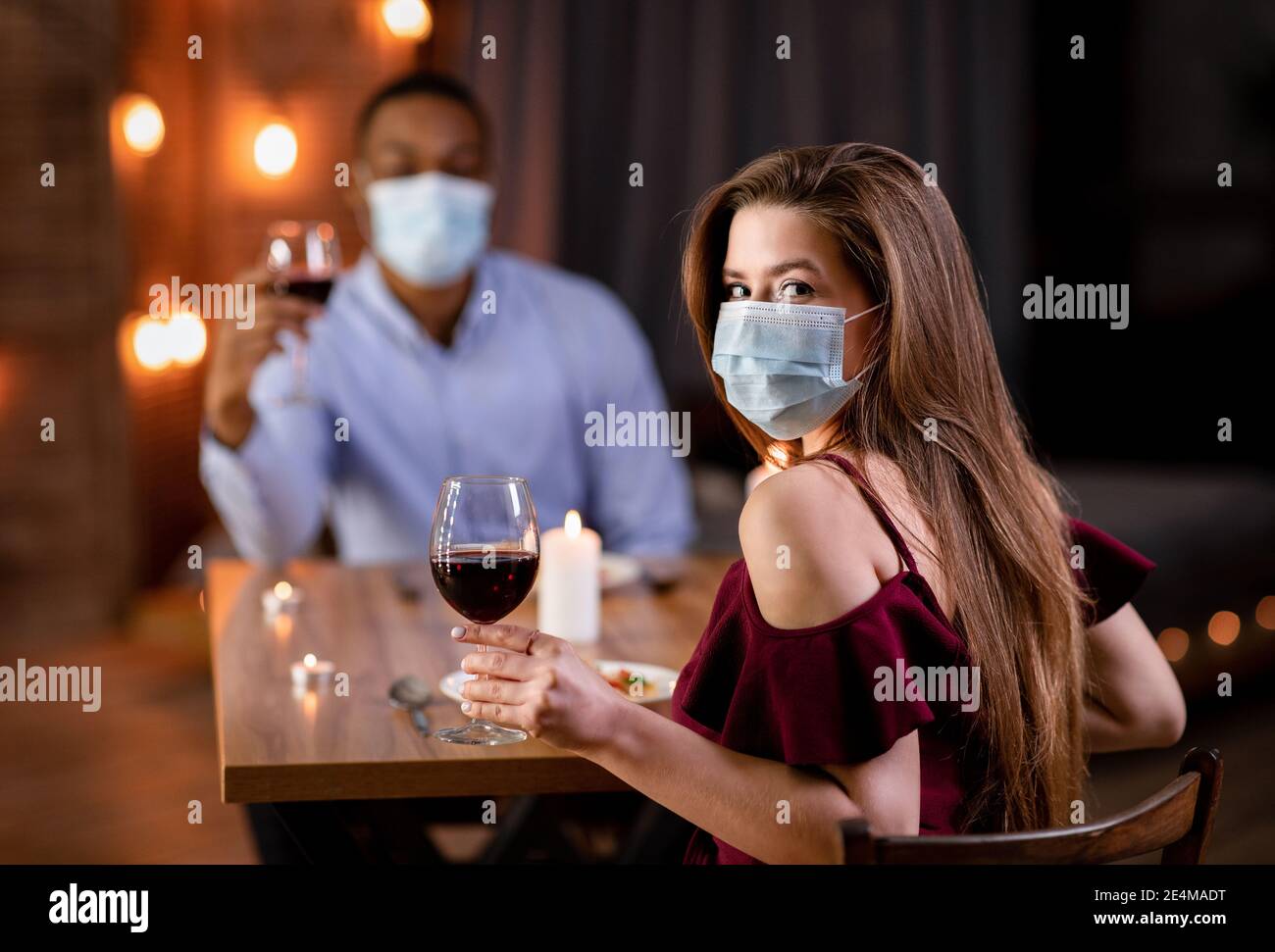 Data pandemia. Giovane coppia Interrazziale in maschere Mediche cena al Ristorante Foto Stock