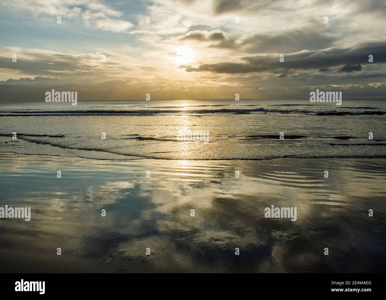Un sole tramontante e una sabbia bagnata piena di riflessi del cielo a Dunraven Bay nel tardo pomeriggio mentre il sole comincia a tramontare. Foto Stock