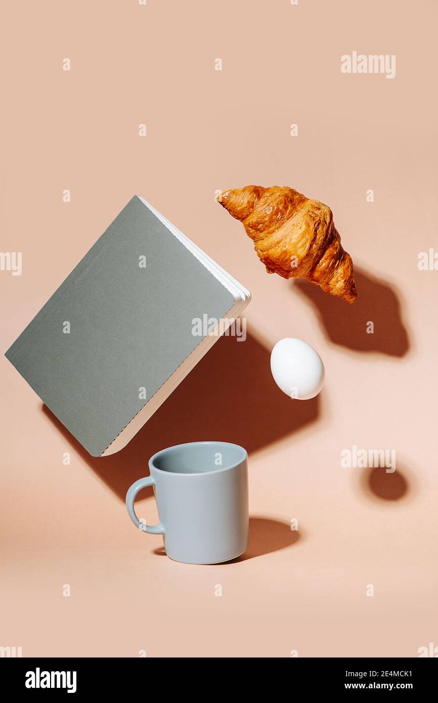 Tazza di caffè sulla superficie color pesca. Croissant, uova e taccuino che si abbiano nell'aria Foto Stock