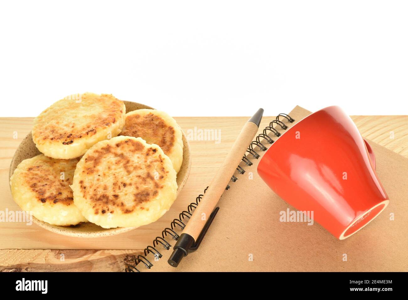 Quattro frittelle intere di formaggio aromatizzate alla bocca che innaffiano, giacciono su un piatto di ceramica, accanto ad esso è una tazza di ceramica rossa con un legno Foto Stock