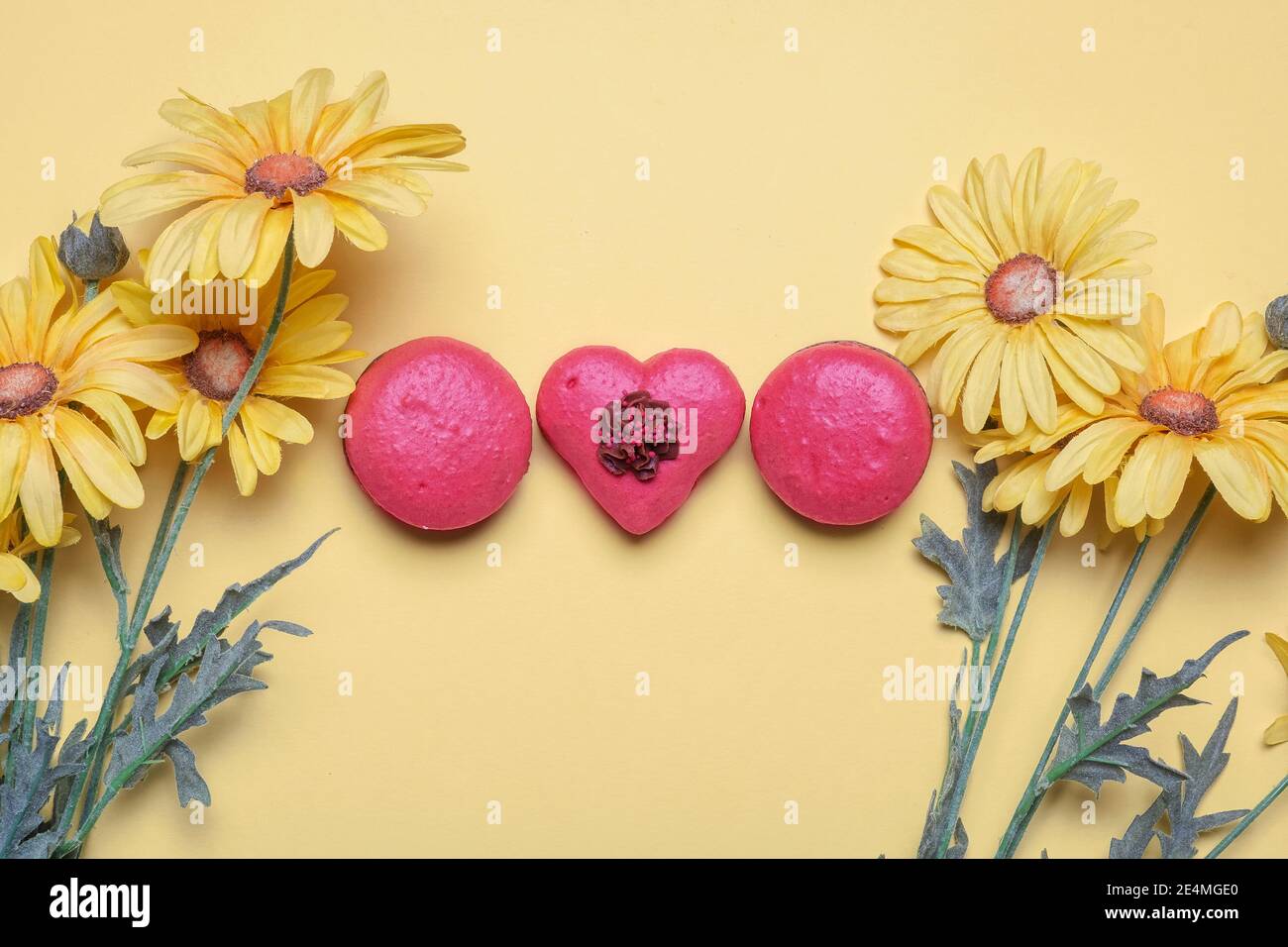 Tre macaroni rossi con un cuore a forma di giallo sfondo con primavera giallo daisy fiori con copia spazio e. spazio per il testo Foto Stock
