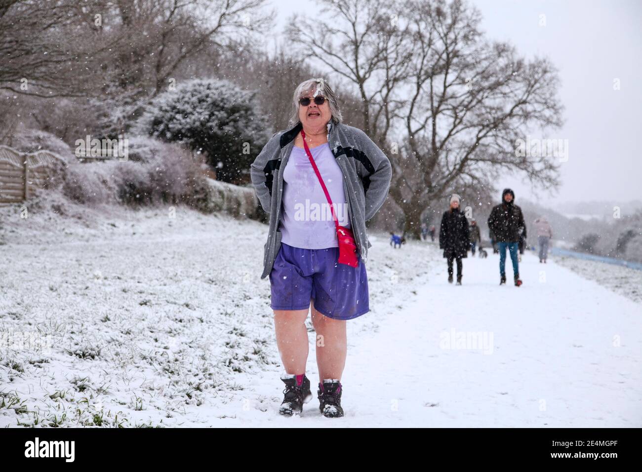 Una donna che indossa pantaloncini e occhiali da sole che cammina in un parco durante una nevicata. Foto Stock