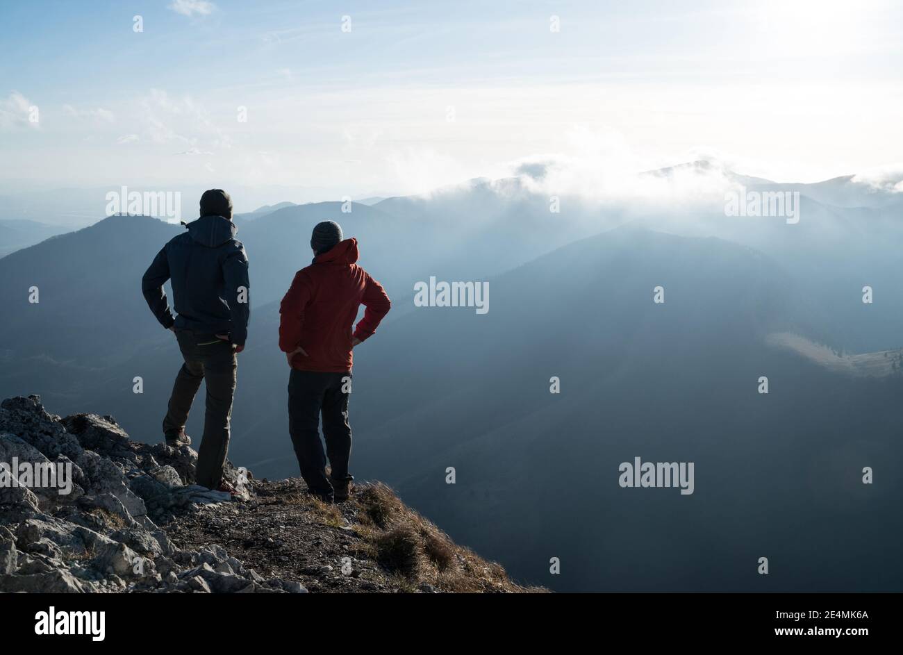 Due uomini in piedi con bastoni da trekking sul bordo della scogliera e guardando il tramonto raggi sulle nuvole. Immagine di successo del concetto di vertice. Foto Stock