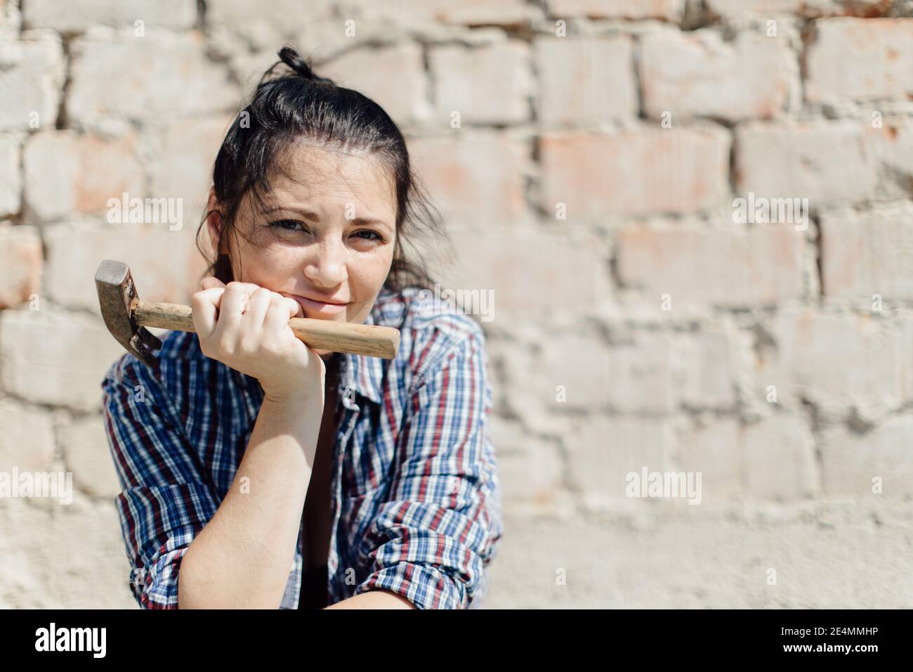 Ritratto di un mento femminile costruttore a portata di mano con un martello contro muro di mattoni Foto Stock