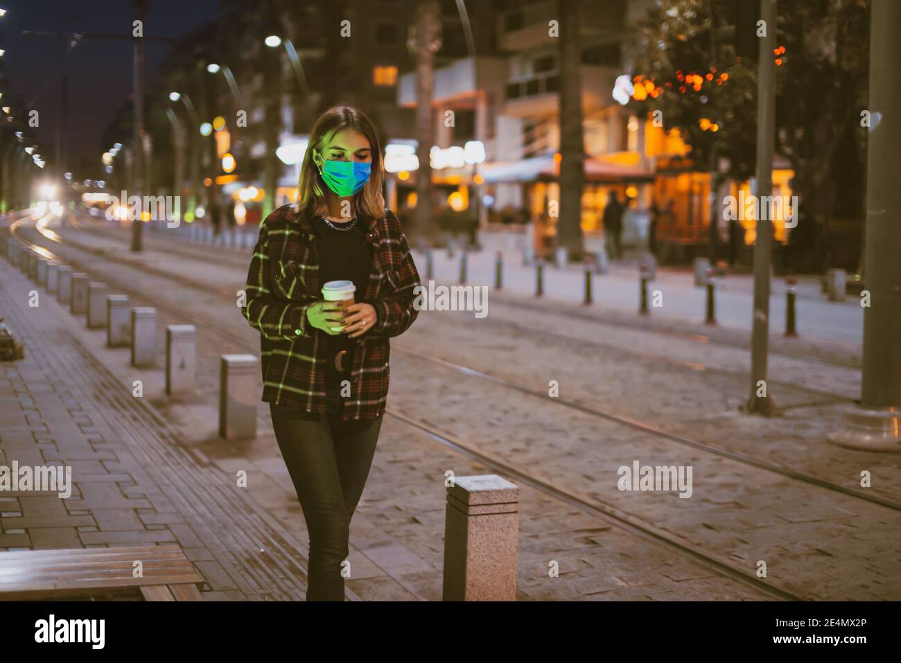 Ragazza adolescente con una maschera medica facciale che cammina su una strada con un take away caffè sulla sua mano. Foto Stock