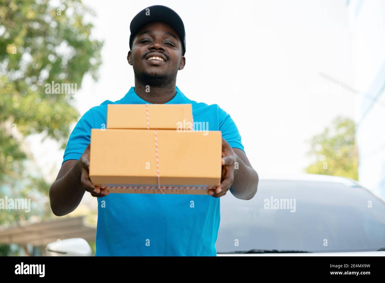 Uomo africano di spedizione postale corriere che tiene consegna scatole di imballaggio di fronte all'auto Foto Stock