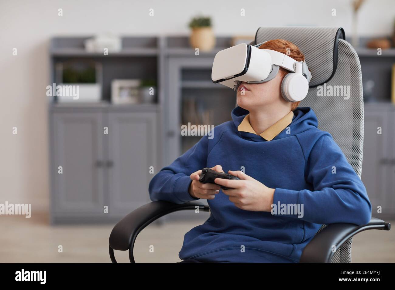 Ritratto di un ragazzo adolescente che indossa un visore VR e tiene il gamepad mentre si gioca a videogame coinvolgenti, spazio di copia Foto Stock