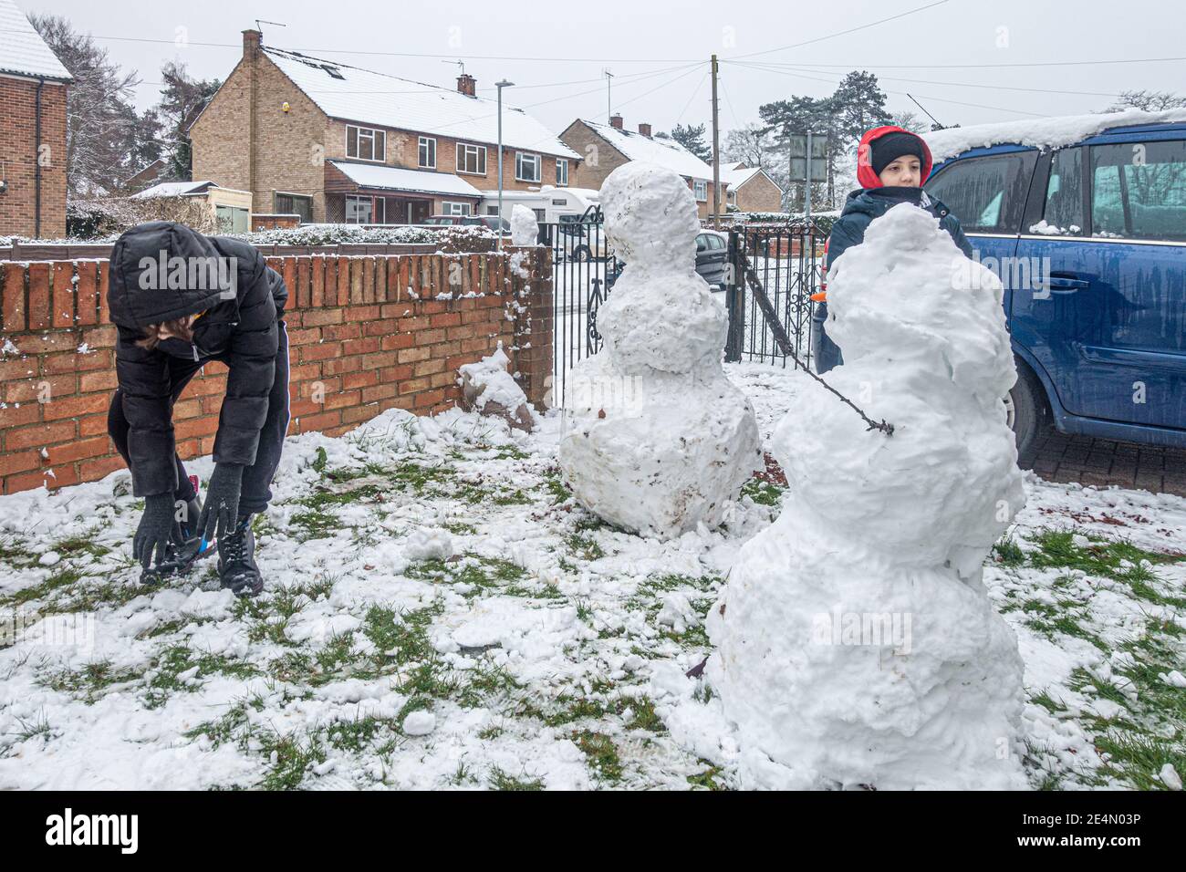 Bambini che costruiscono un pupazzo di neve in un giardino anteriore a Reading, Regno Unito dopo la prima nevicata dell'inverno. Foto Stock