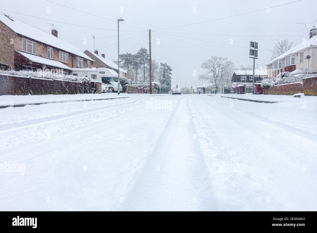 Una strada residenziale a Reading, Berkshire, Regno Unito è coperta di neve. Le piste dell'auto conducono in lontananza. Foto Stock