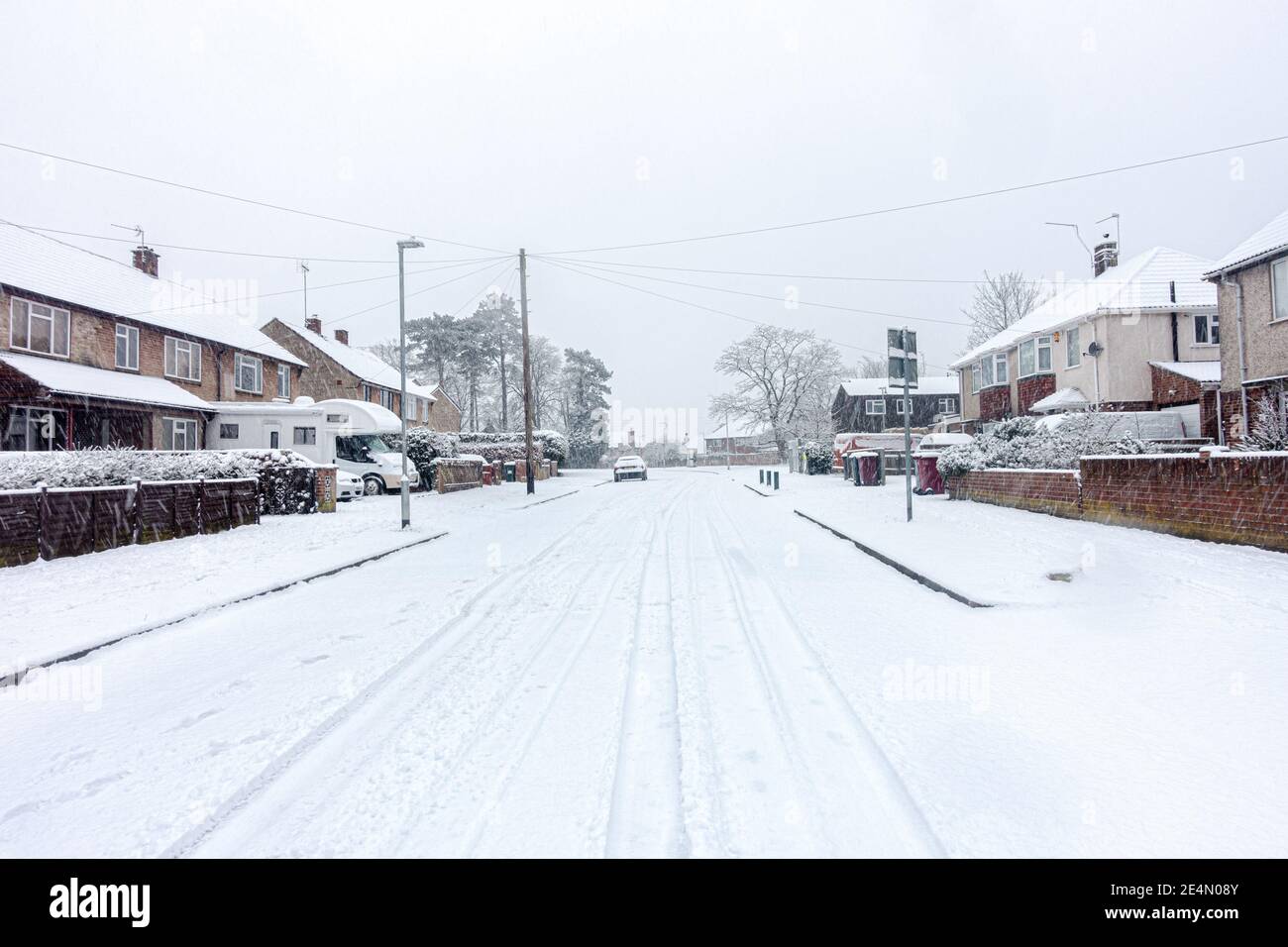 Una strada residenziale a Reading, Berkshire, Regno Unito è coperta di neve. Le piste dell'auto conducono in lontananza. Foto Stock