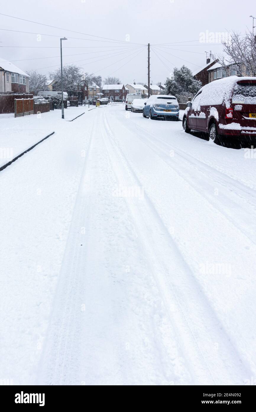 Una strada residenziale a Reading, Berkshire, Regno Unito è coperta di neve. Le piste dell'auto conducono in lontananza. Foto Stock