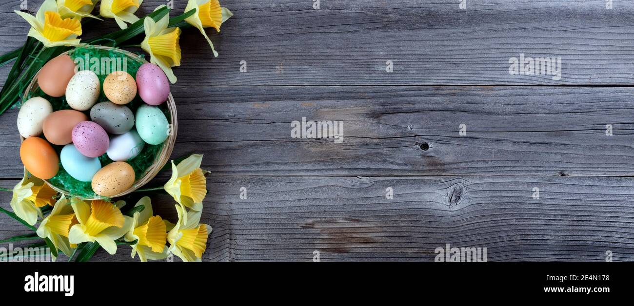 Buon passato di Pasqua con cesto tradizionale pieno di colori uova e erba verde più fiori di daffodil su legno rustico tavole Foto Stock