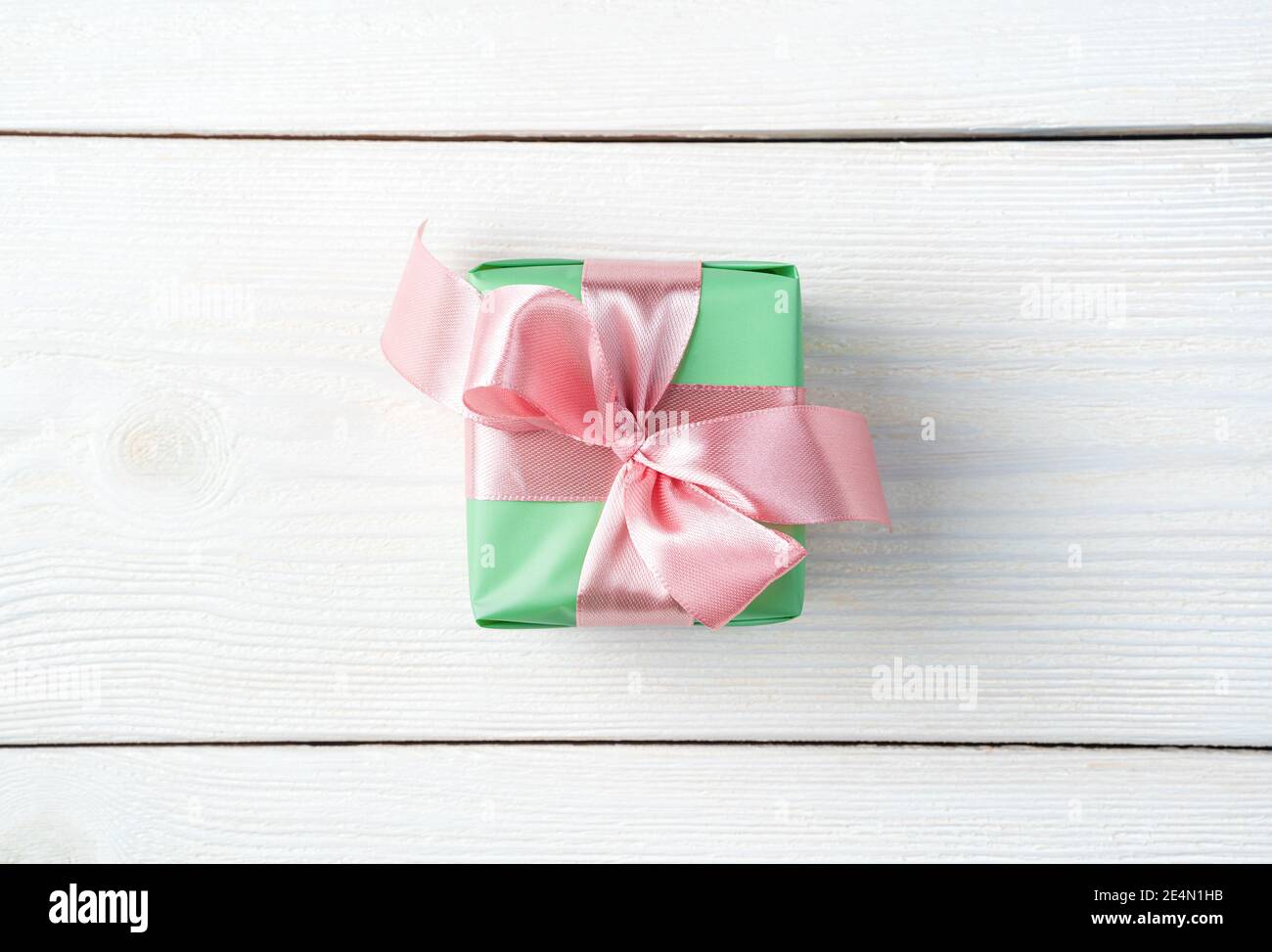 Confezione regalo verde con nastro rosa su sfondo bianco di legno. Foto Stock