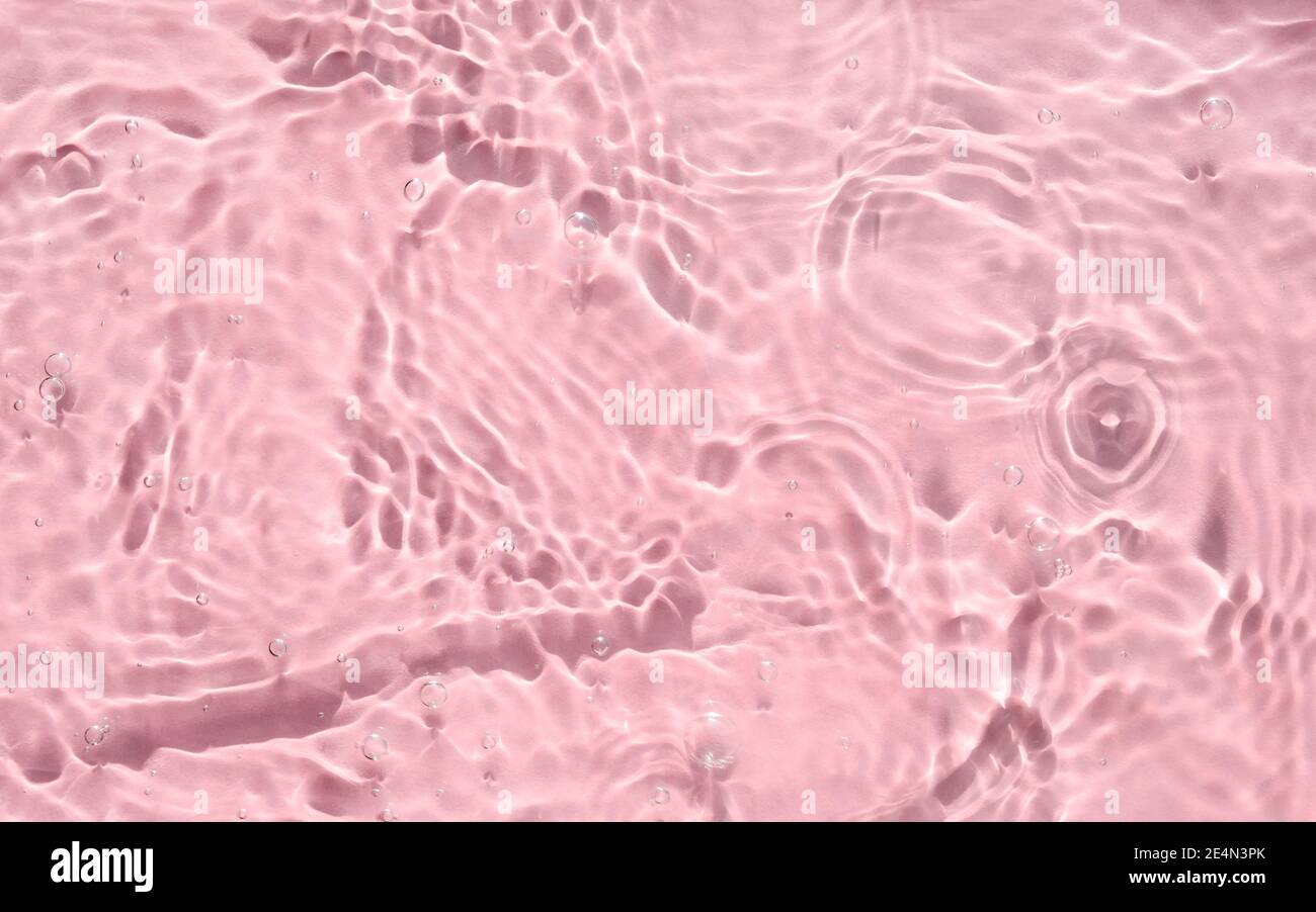 Consistenza d'acqua rosa con increspature, onde e bolle. Primo piano di riflessi solari e ombre su una superficie d'acqua testurizzata. Retrogrun estivo astratto alla moda Foto Stock