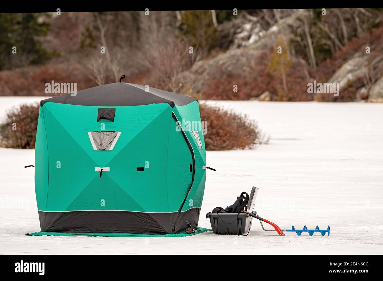 Una tenda di pesca sul ghiaccio verde su un lago ghiacciato. Trapano di ghiaccio e altre attrezzature vicino alla tenda. Shore dietro. Nessun marchio. Foto Stock