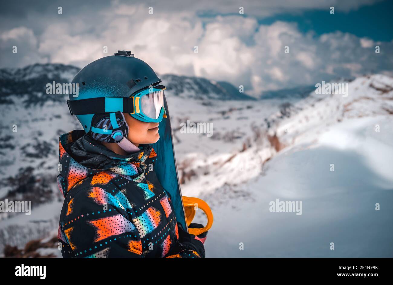 Profilo Ritratto di Snowboarder Girl guarda in lontananza in un bellissimo paesaggio invernale di montagna. Persone attive che apprezzano la stazione sciistica. Foto Stock