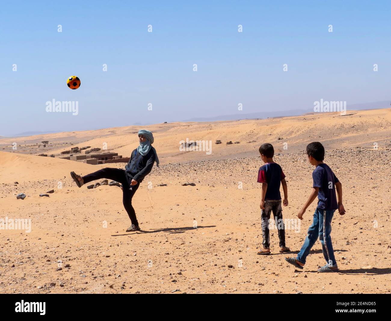 Bambini marocchini che giocano a calcio con una palla nell'estate del deserto del Sahara. Foto Stock
