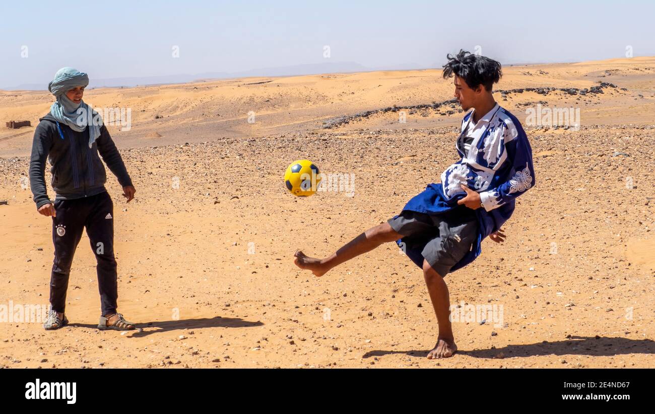 Bambini marocchini che giocano a calcio con una palla nell'estate del deserto del Sahara. Foto Stock