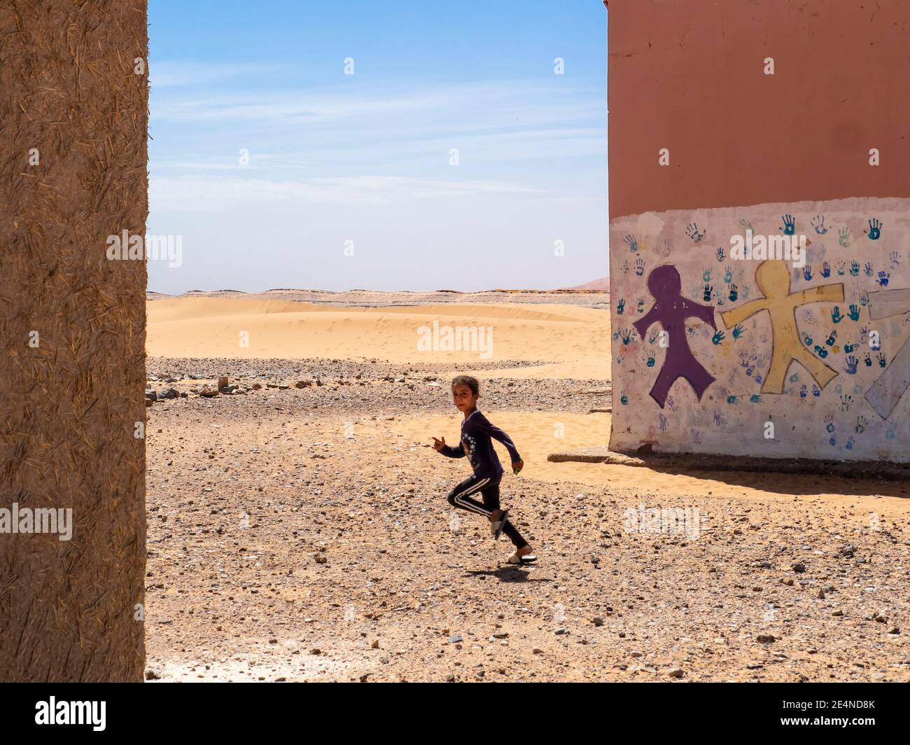 La ragazza marocchina corre tra due edifici scolastici nel Sahara deserto in estate Foto Stock