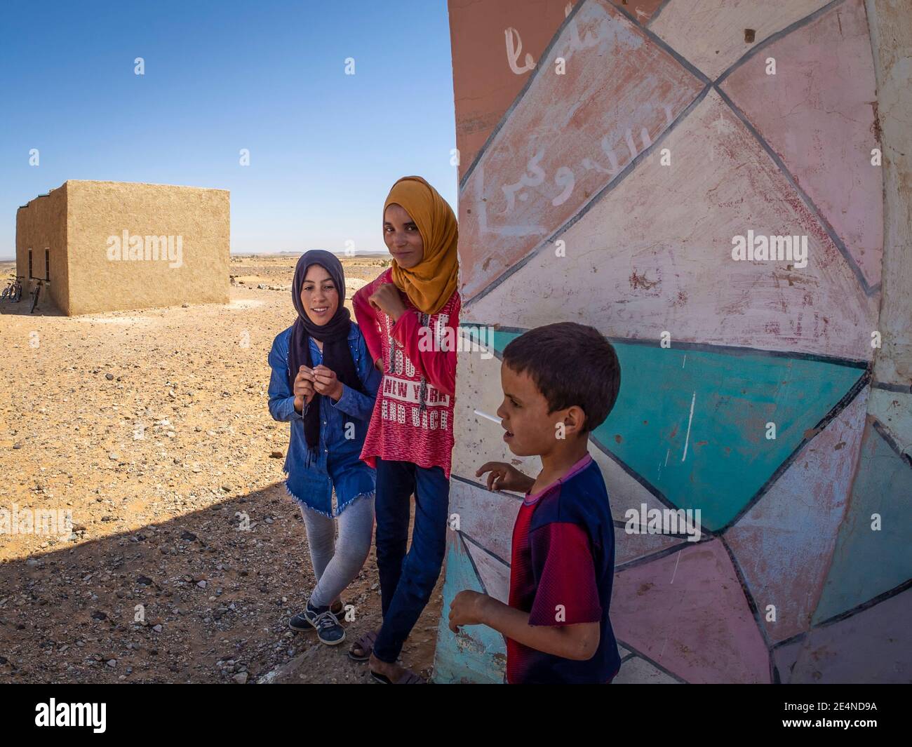 Tre alunni di una scuola nel deserto marocchino si rompono all'ombra delle alte temperature estive. Foto Stock