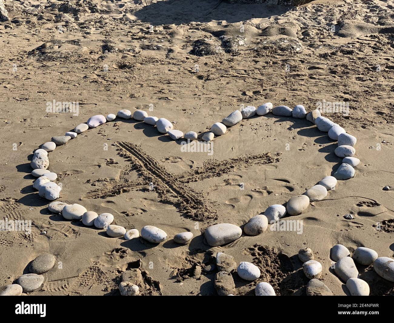 Un cuore fatto di rocce su una spiaggia sabbiosa con Un segno X al centro Foto Stock