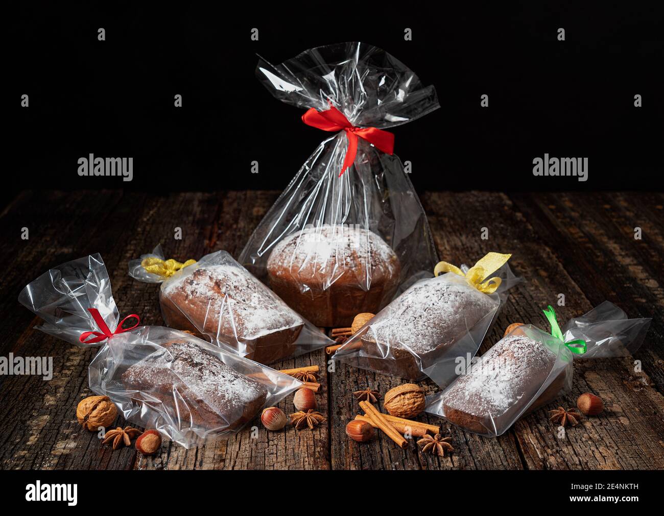 Regalo di Natale pane stollen, in confezione di plastica e un nastro, steso su una tavola e un tavolo di legno, con noci e spezie. Foto Stock