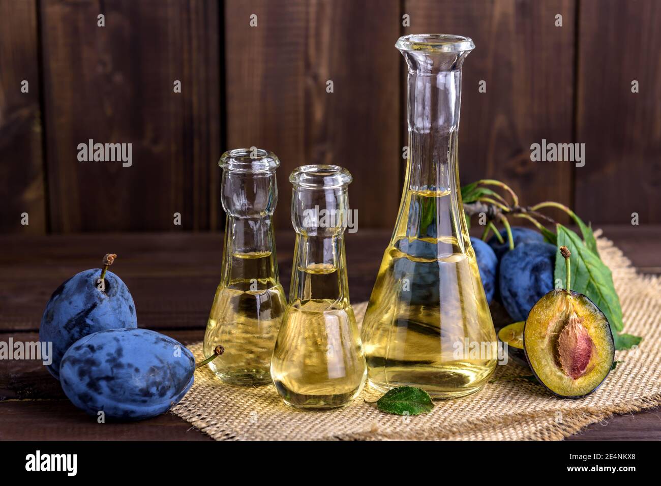 Brandy di prugne o schnapps in piccole bottiglie di vetro con prugne fresche e gustose su un tavolo di legno. Messa a fuoco selettiva. Foto Stock