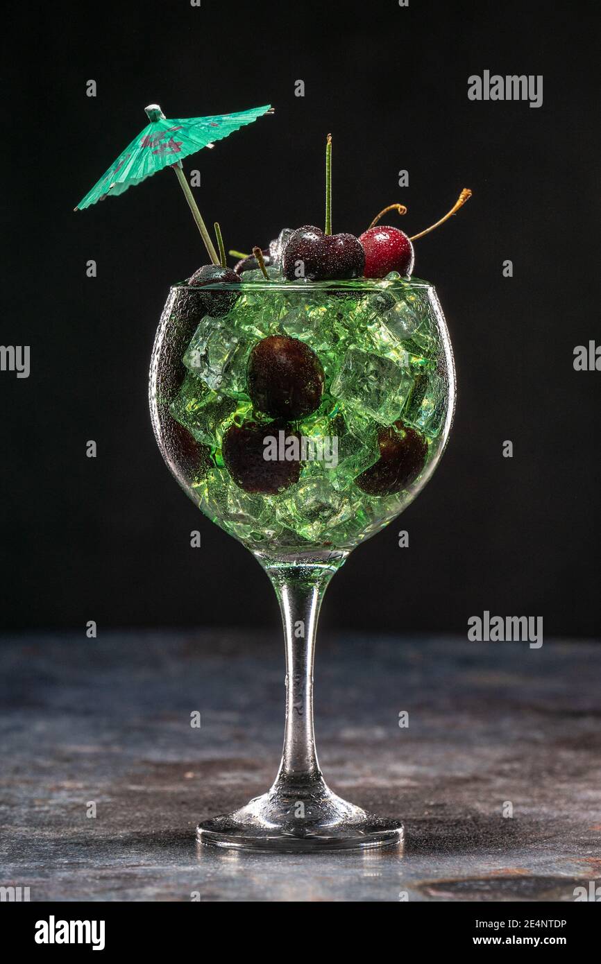 Cocktail verde con ghiaccio e ciliegie in vetro decorato con ombrelloni Foto Stock
