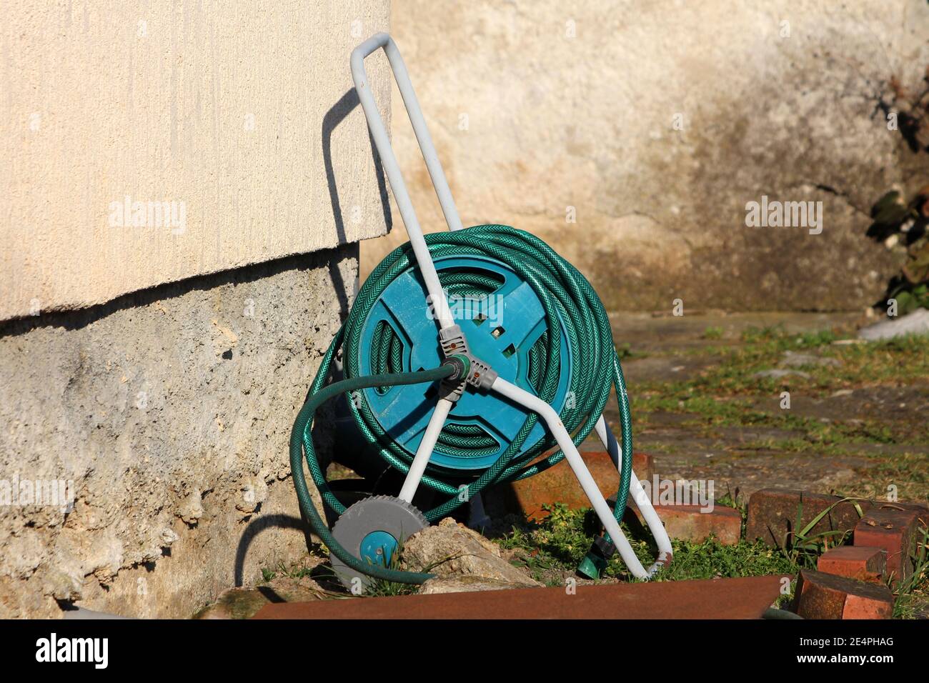 Lungo tubo da giardino verde scuro montato su avvolgitubo da giardino con ruote piccole per un trasferimento più facile in casa di famiglia cortile accanto alla parete della casa Foto Stock