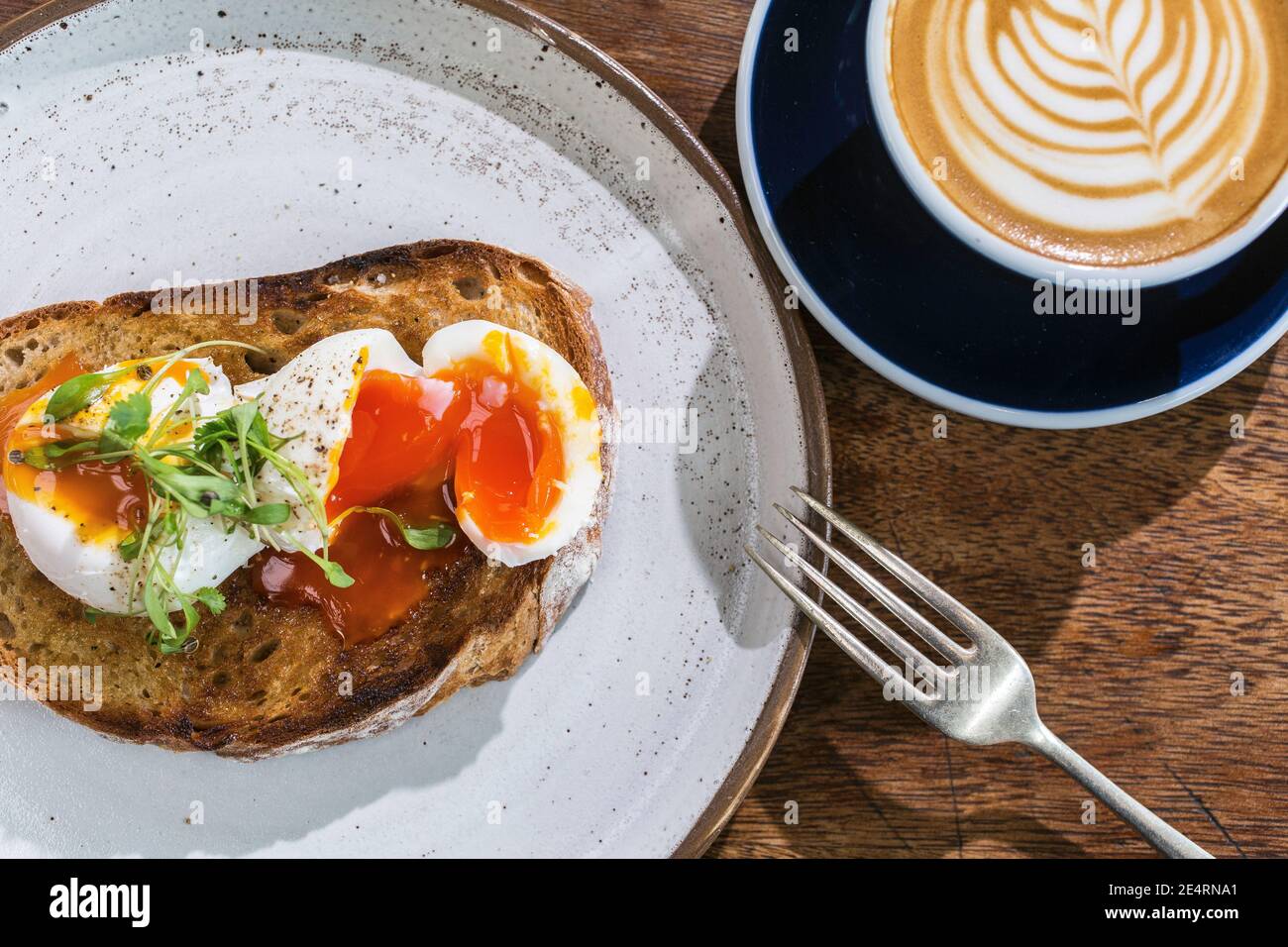 Una tazza di caffè con latte art sulla parte superiore, pane tostato di impasto con uova in camicia sul tavolo in caffea. Foto Stock