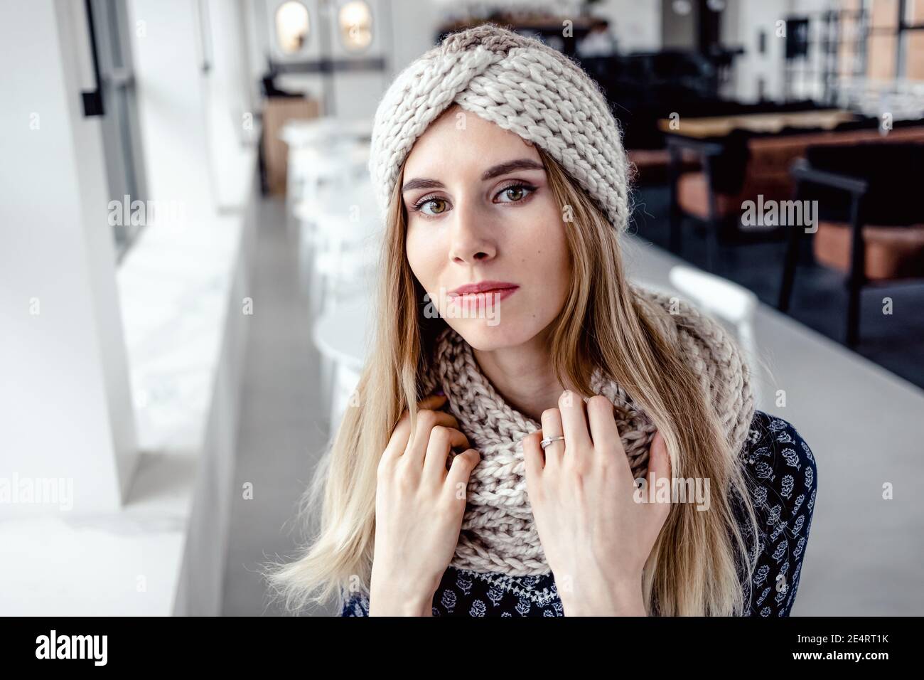 Bella donna carina che indossa cappello e sciarpa in maglia invernale sullo sfondo del cafe. Foto Stock