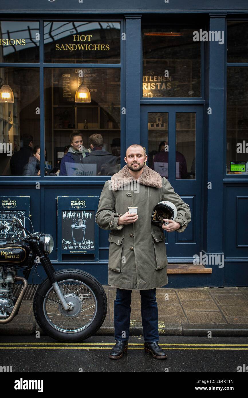 Un uomo fa una pausa caffè in un caffè in Londra con moto classiche parcheggiate di fronte ad un caffè negozio Foto Stock