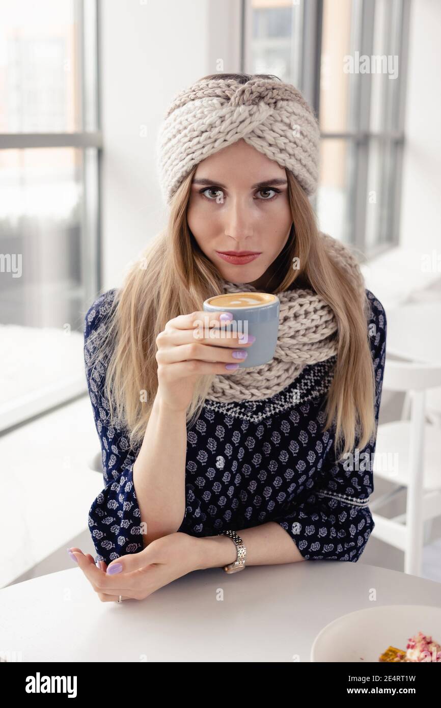 Bella ragazza d'inverno carina che indossa cappello e guanti in maglia con tazza da caffè. Ragazza attraente con bevanda calda sullo sfondo del caffè. Bere caffè e en Foto Stock